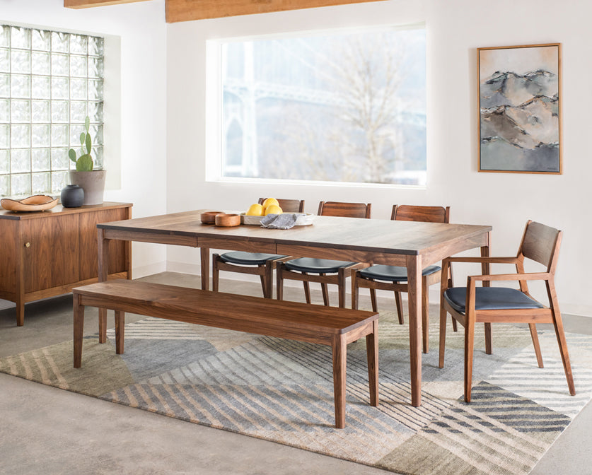 Dining room with wooden table, chairs, and bench on a patterned rug.