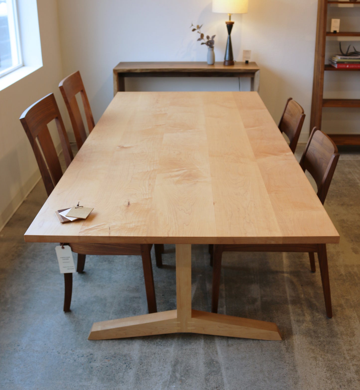 Wooden dining table with four chairs in a room with a lamp and shelves.