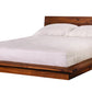 A modern platform bed with a dark Walnut wood frame and headboard, dressed in white bedding and pillows, shown against a plain white background.
