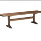 A rustic wooden dining bench with a medium brown wood grain finish, featuring a thick rectangular seat and a sturdy support frame with angled feet, shown against a plain white background.