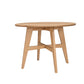 A light natural oak wood dining table with a round top and four angled legs connected by a central X-brace, shown on a plain white background.