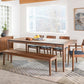 Dining room with wooden table, chairs, and bench on a patterned rug.