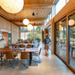 Modern office interior with wooden tables and chairs, large windows, and a person walking.