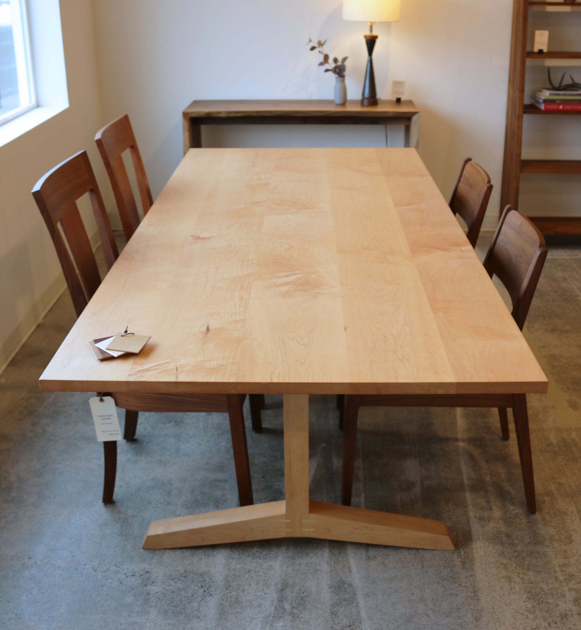 Wooden dining table with four chairs in a room with a lamp and shelves.