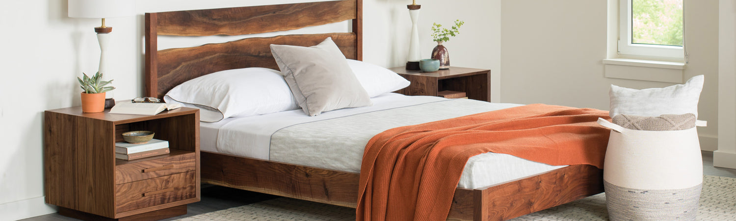 Modern Live Edge Split Bed, shown in a modern bedroom featuring white bedding, an orange blanket, two bedside tables with lamps, and decorative plants, set against a light wall and window.