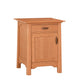 A small wooden nightstand with a warm honey oak finish, featuring a single drawer with a dark wood pull and a single cabinet door with a matching dark wood pull, set against a plain white background.