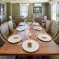 Dining room with a long wooden table set for a meal, surrounded by upholstered chairs.