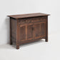 A rustic dark brown wooden sideboard cabinet with two drawers on top and two paneled doors below, set against a plain white wall and floor.