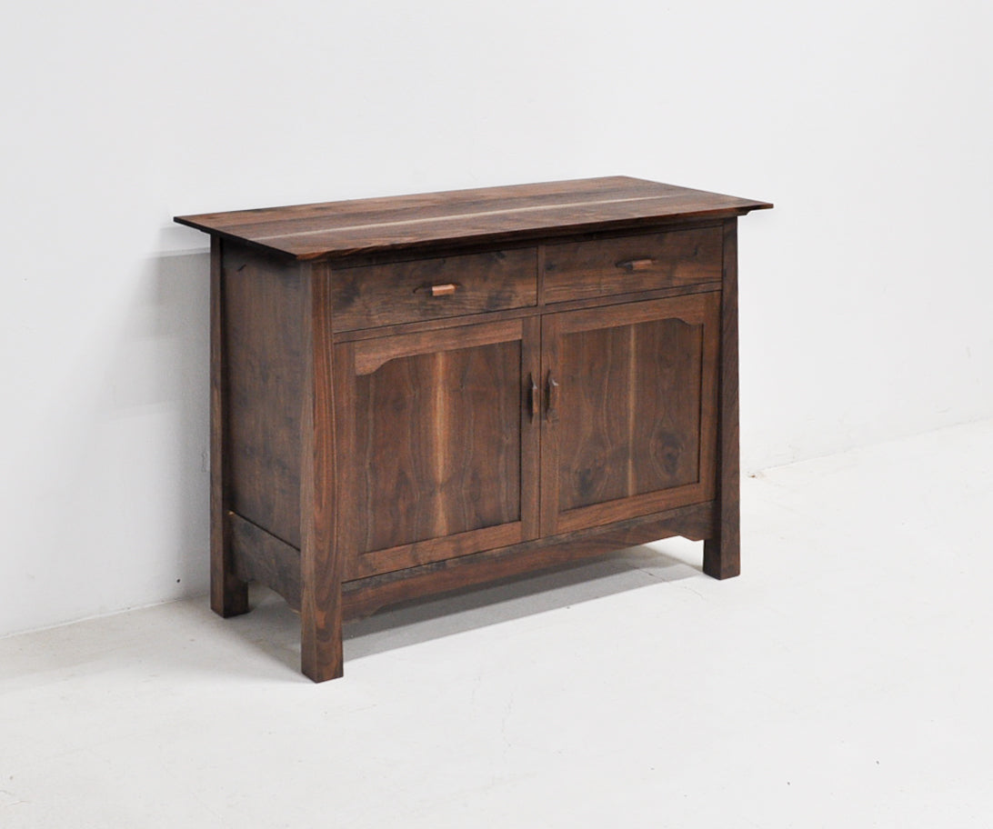 A rustic dark brown wooden sideboard cabinet with two drawers on top and two paneled doors below, set against a plain white wall and floor.
