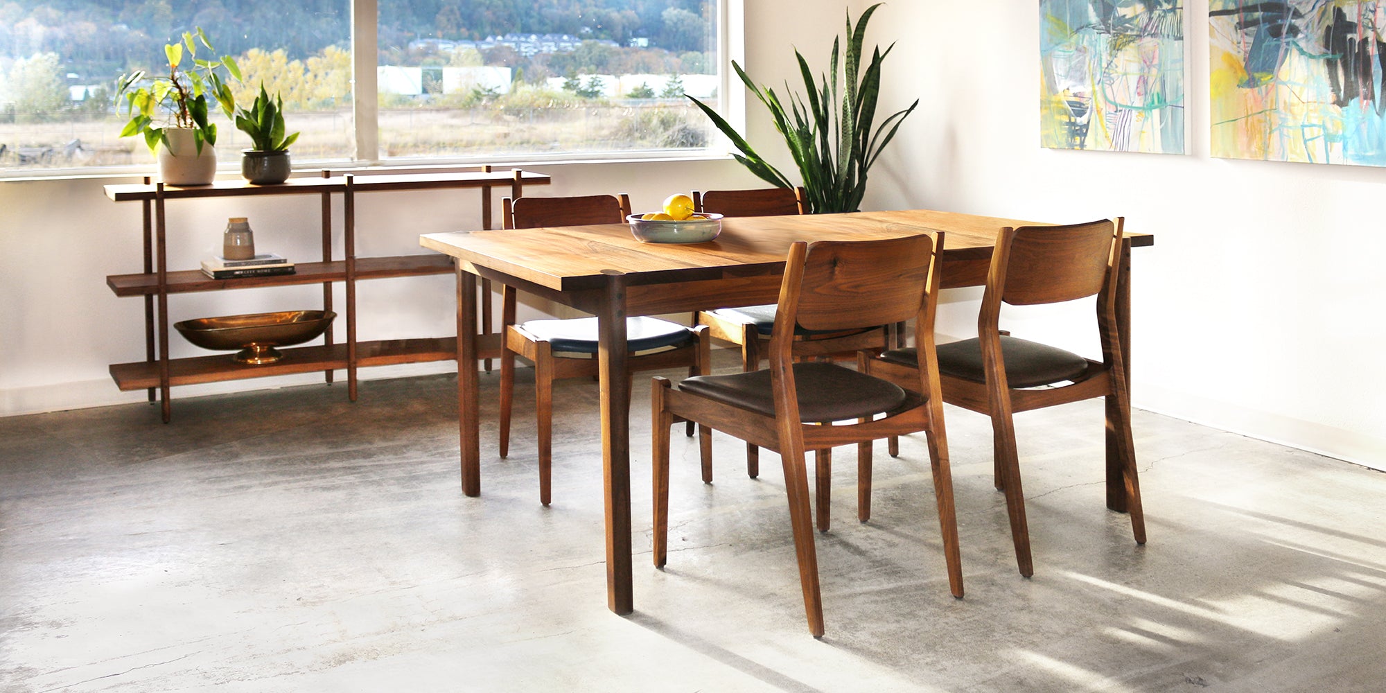 Sebastian Dining Table by The Joinery in Walnut with bookcase behind i