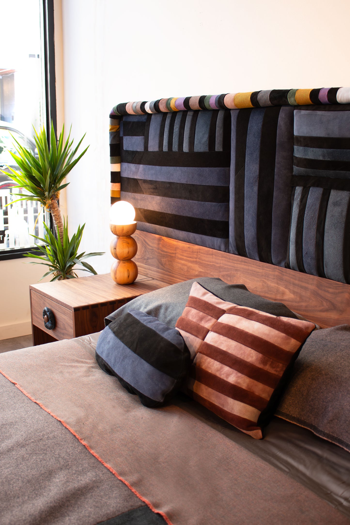Bedroom with a bed featuring patterned headboard and pillows, nightstand with lamp, and plants.