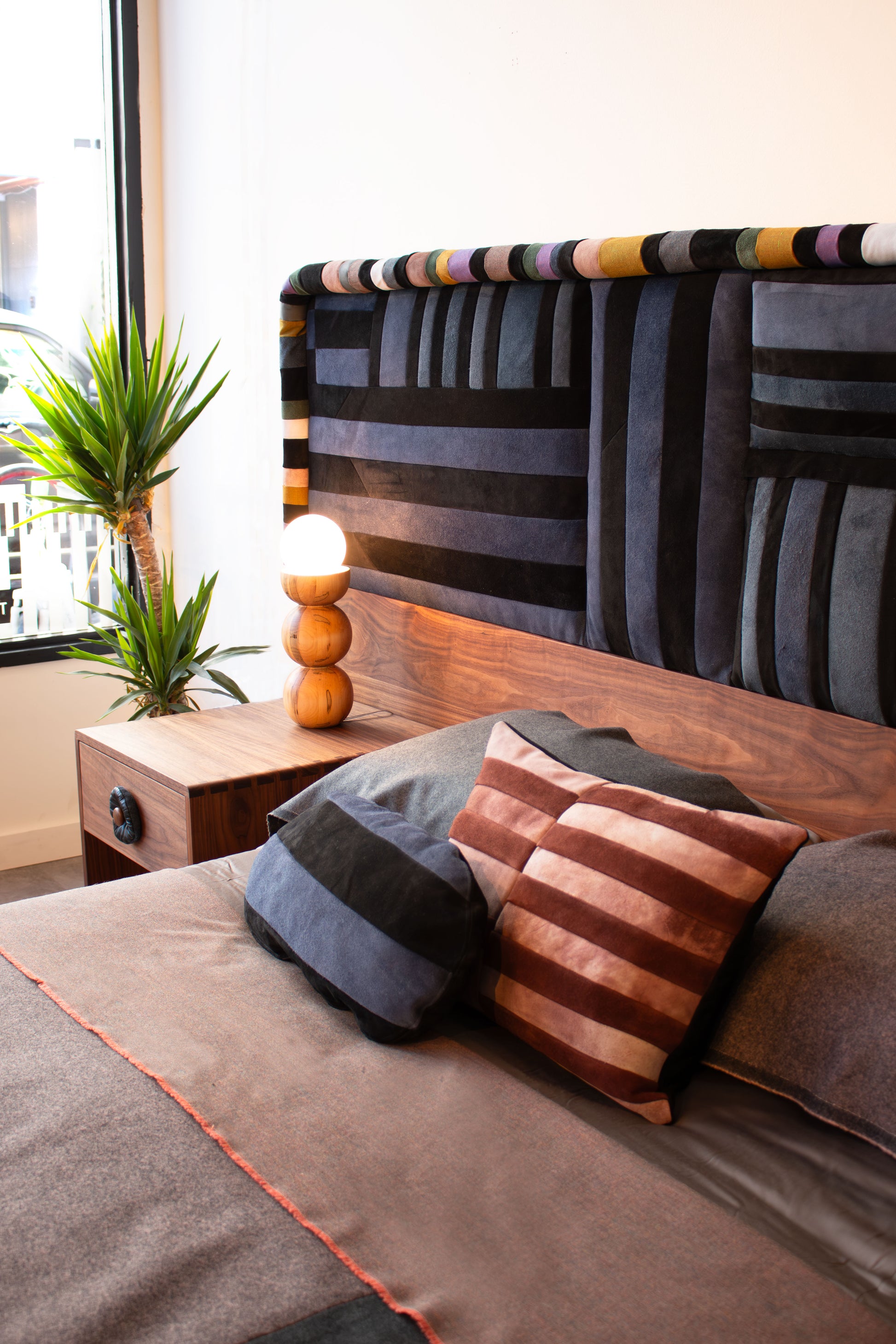 Bedroom with a bed featuring patterned headboard and pillows, nightstand with lamp, and plants.