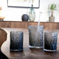 Set of three textured glass tumblers on a wooden surface with a blurred indoor background.