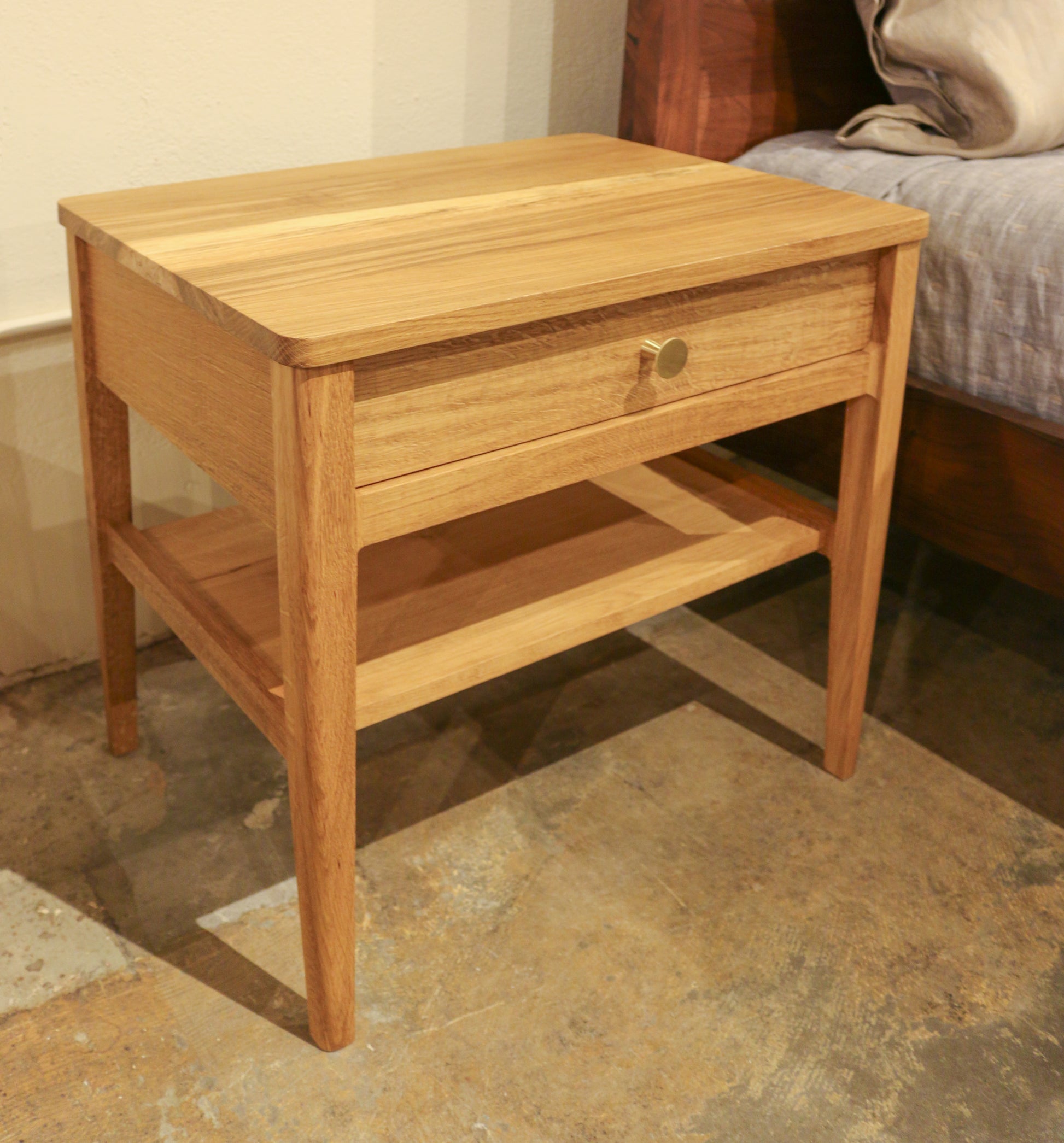 Wooden nightstand with a drawer next to a bed in a bedroom setting