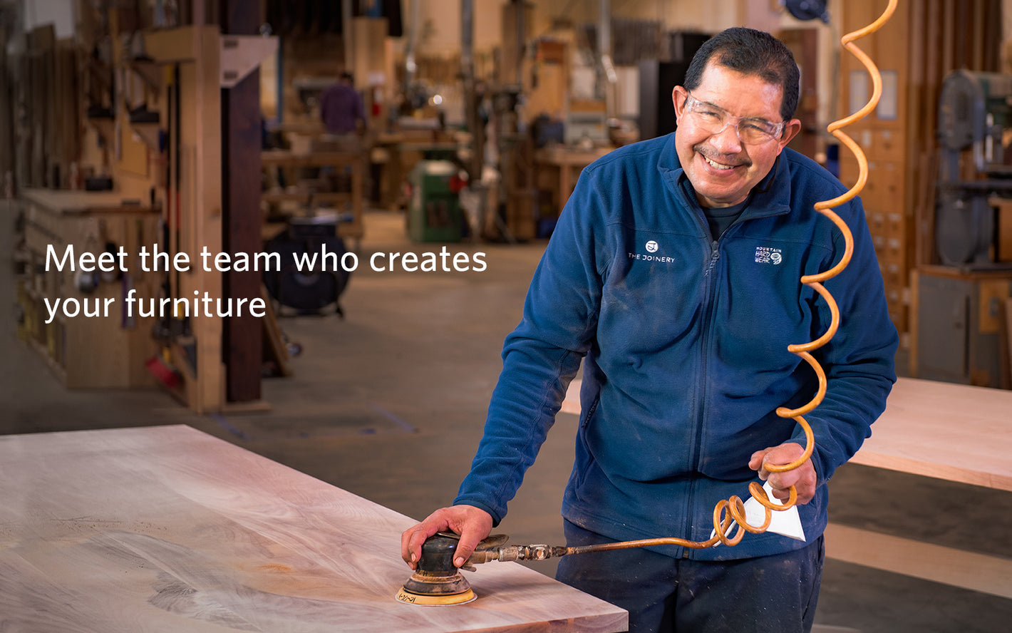 Image of The Joinery finisher, Angel as he sands a dining table in a woodshop